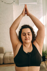 A young curly-haired plus-size woman meditating at home,doing breathing exercises.Healthy lifestyle.