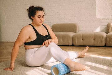 A young plus-size woman using a foam roller to massage the leg muscles.Myofascial...