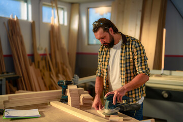 Carpenter carefully sands wooden plank with electric sander, surrounded by tools and lumber in his...