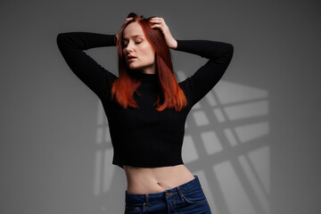 Redhead woman posing on grey background with abstracted shadow