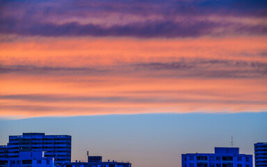 Orange clouds in blue sky over city buildings at sunset