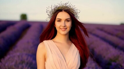 A beautiful woman with long, flowing auburn hair standing in a vast, vibrant lavender field. She wears a flowing pink dress that complements the soft purple hues of the flowers. - Powered by Adobe