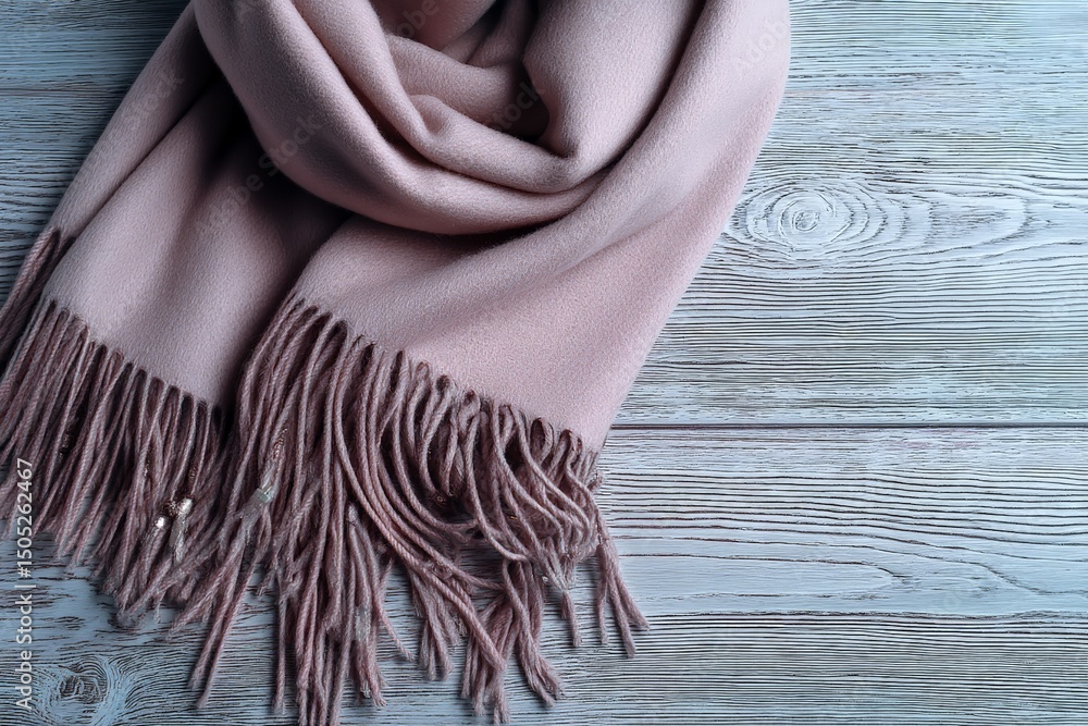 Poster soft pink scarf neatly arranged on a wooden surface with delicate fringes and subtle detail
