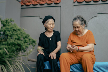 Two elderly women sharing stories in a peaceful courtyard during the afternoon in a traditional...