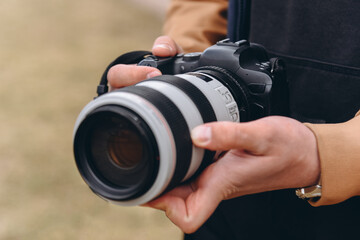 black and white dslr camera in hands, large long lens, young caucasian man photographer at work outdoors in sunny summer day
