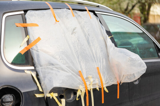 Damaged rear car window temporarily covered with plastic sheet and tape, serving as a quick fix for weather protection.