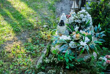 Beautiful floral arrangement on a green cemetery grave with white roses and lush foliage near...