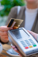 Close-up view of a person making a contactless payment using a credit card on a POS terminal. The scene takes place in a cafe setting with a teapot in the background, showing modern transaction ease 
