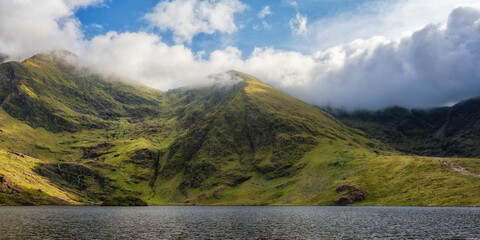 Lough Callee showcases stunning emerald hills enveloped in clouds, creating a serene natural vista. The calm waters mirror the landscape, highlighting Ireland's scenic charm.