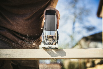 man saws a wooden slat in the garden with a cordless jigsaw