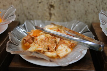 Putting homemade kimchi, a Korean heritage dish, into a small bowl with wooden serving tongs.