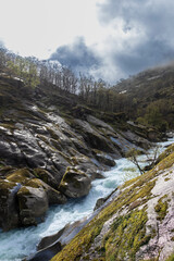River flowing through rocky mountain valley under cloudy sky