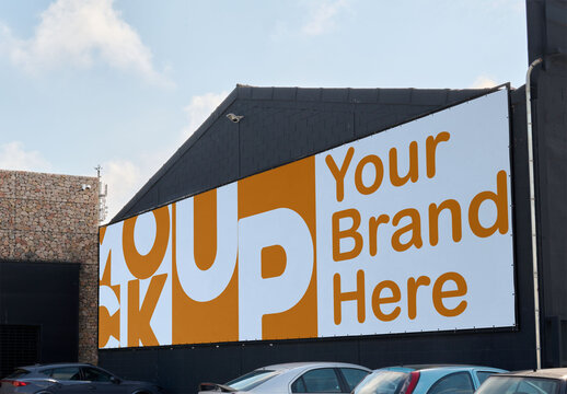 A blank billboard mockup set on a building wall near parked cars.