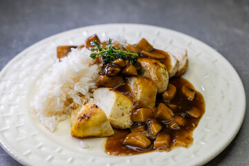 Sliced chicken breast with mushroom sauce and rice on white plate