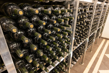 Wine bottles aging on metal shelves in cellar with tiled floor
