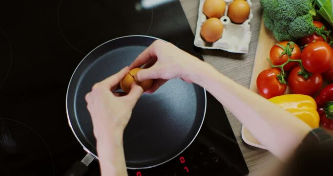 Close up woman hands cracking egg into frying pan. High angle view.