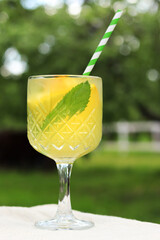 Close-up of a glass with a cocktail outdoors. Lemonade on a blurred nature background. Lemonade or other drink in a glass. Summer refreshing drink with mint and orange slices