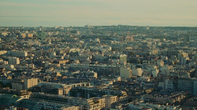 Aerial view of a densely packed Parisian residential district at sunset, showing layers of mid-rise buildings, rooftops, and modern towers fading into the hills.