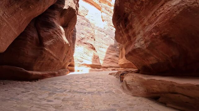Ancient paved road among the sandstone rocks. Low angle view at the air-cut Al Siq Canyon in Petra, Southern Jordan, West Asia.