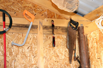 Tools and building materials on a wooden wall of a barn, saw, hacksaw, cable, rope, screwdriver,...