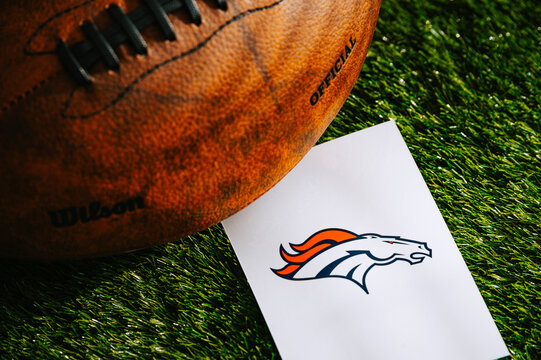 Denver Broncos team Logo and American football ball on Green Grass.