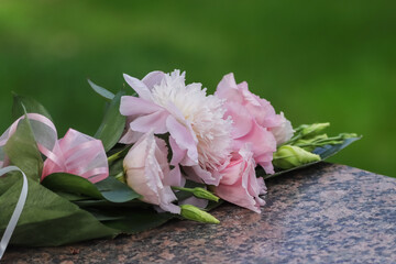 Single bouquet of flowers on a cemetery memorial stone. Beautiful bouquet of pink flowers tied with a decorative ribbon. Blurred green background.