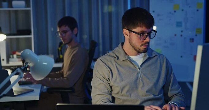 Team adult male freelance developer work late typing write prompt AI bot app program nomad terminal code at office night. Artificial intelligence dashboard, robotics, user interface, machine learning.