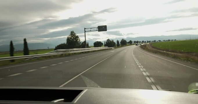 A subjective shot taken from inside the vehicle while driving shows a road with cars passing by, a blue sky and a green field.