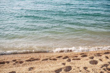 A sea with little waves crashing against the shore. The sandy beach is visible in the foreground