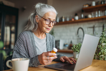 Senior woman using laptop computer to research medication refills online from home kitchen