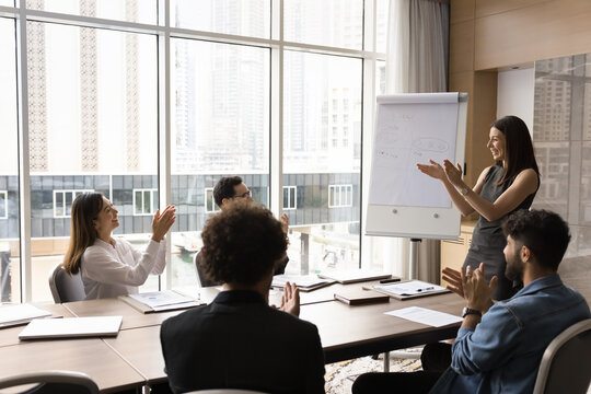 It deserves applause. Happy motivated multiethnic corporate team lead by female boss gather on meeting at conference room table clapping hands celebrate successful result of cooperation teamwork event