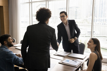 Fototapeta na wymiar Closing deal. Smiling male business partners shake hands in presence of happy diverse stakeholders on meeting make financial agreement conclude procurement contract satisfied with negotiations result