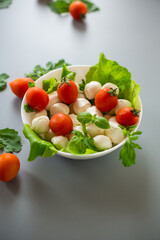 White bowl with mini mozzarella and greens on a gray background