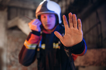 No trespassing, stop hand gesture. Firefighter in professional equipment is indoors in abandoned...
