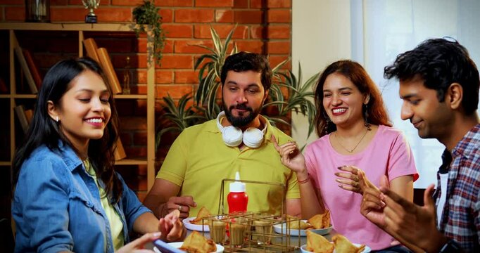 Taking selfie having samosa and chai in cafe, Indian college students enjoying snack together while capturing joyful group photo using smartphone in casual indoor restaurant setting with friends