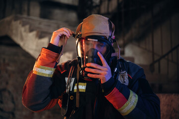 Ready, using a mask. Firefighter in professional equipment is indoors in abandoned building
