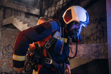 Obraz premium Adjusting air flow into the mask. Firefighter in professional equipment is indoors in abandoned building