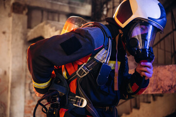 Naklejka premium Hard to breathe, using air mask. Firefighter in professional equipment is indoors in abandoned building