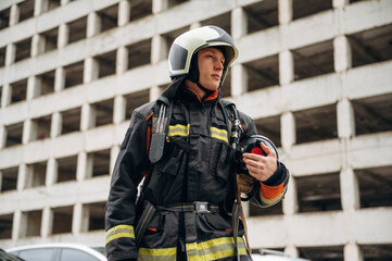 Fototapeta premium Professional firefighter is standing outdoors against big unfinished building