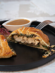 A plate of chicken wellington cut in a half piece, stuffing with mushroom and spinach with poultry sauce, shitake mushroom, beetroots sprout as a side dish.