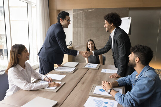 Business partnership. Two young men in formal suits ceo top managers leaders handshaking on board of directors meeting negotiate contract enjoy collaboration agree on merger acquisition deal welcome