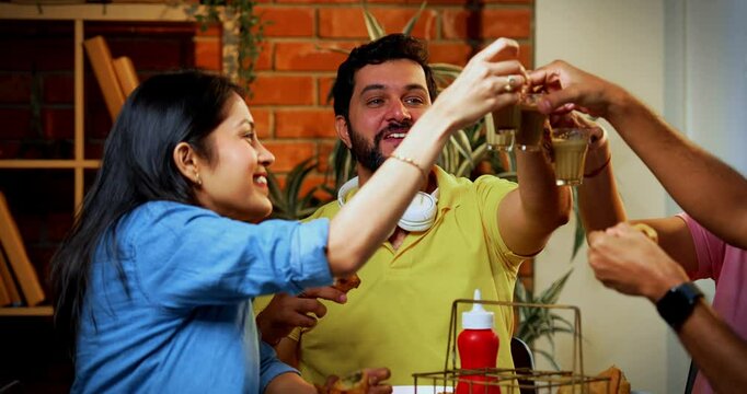 Eating samosa and sipping chai in cafe, Indian Asian young college friends having fun reunion while enjoying snacks, laughing and bonding together indoors at cozy restaurant or canteen setting