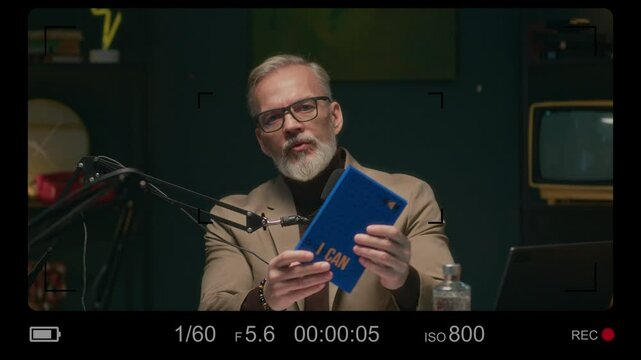 Stab camera recording screen view of mature Caucasian author talking about his book during online podcast in studio