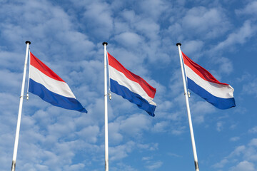 Three Dutch flags waving proudly against a partly cloudy blue sky. A patriotic and serene scene representing the Netherlands and national identity.