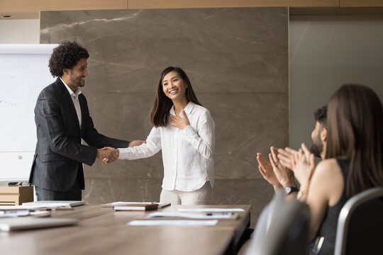 I am flattered. Smiling team leader chief shake hand of grateful happy young coworker teammate on conference event praise for professional achievement appreciate good work before applauding audience
