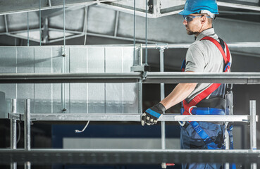 Worker in Safety Gear Installs HVAC System in Industrial Building During Daytime Projects