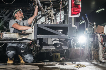 Mechanic Repairing Vehicle Undercarriage in Dimly Lit Workshop During Day