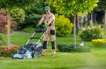 Lawn Care Expert Mows Grass in a Lush Garden During a Sunny Afternoon in Early Spring