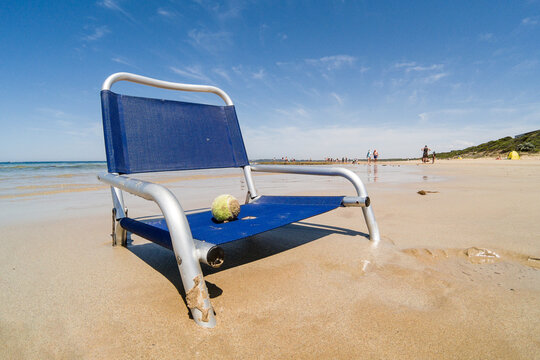 A tennis ball sitting a beach chair sunken into the sand on a beach