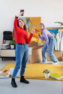 Two happy young women take a celebratory selfie during a move. One makes a peace sign, the other gives a thumbs-up, sharing their excitement about the new place.